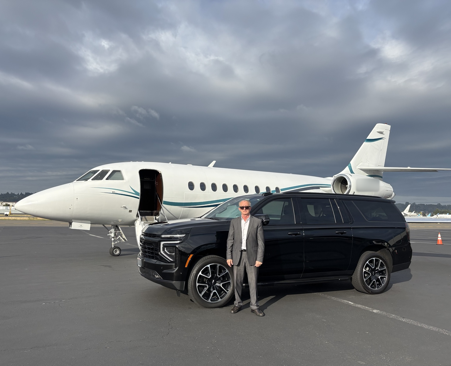 Easy Driven owner beside a black Chevrolet Suburban and private aircraft